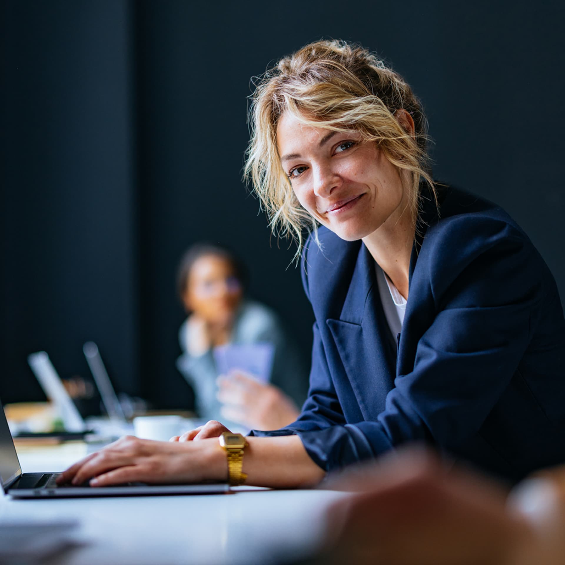 A confident mortgage adviser with a warm smile sitting at a table with a laptop, portraying positivity in her workplace environment.