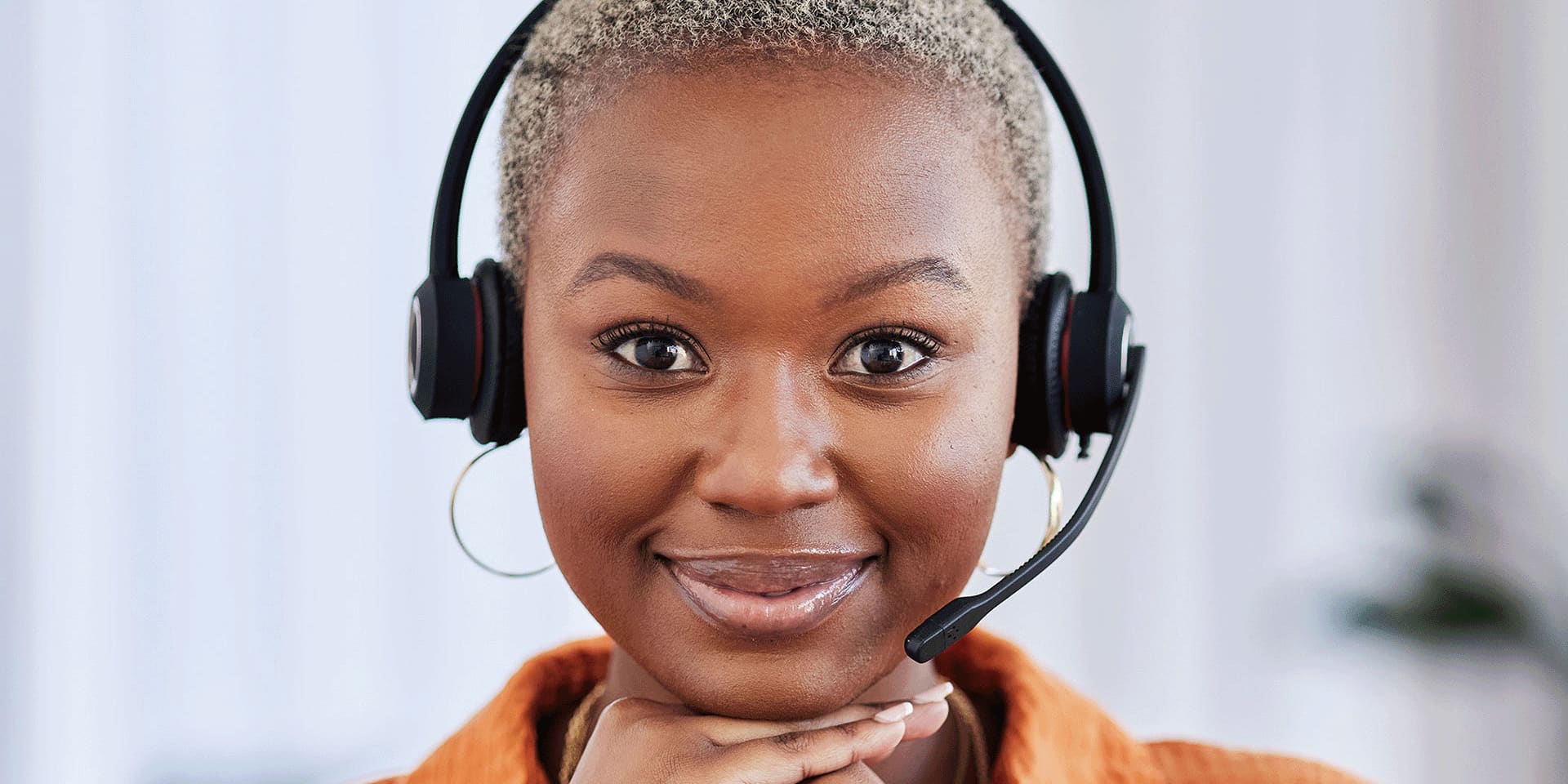 Young woman sitting wearing a headset and her hands on her chin, smiling.