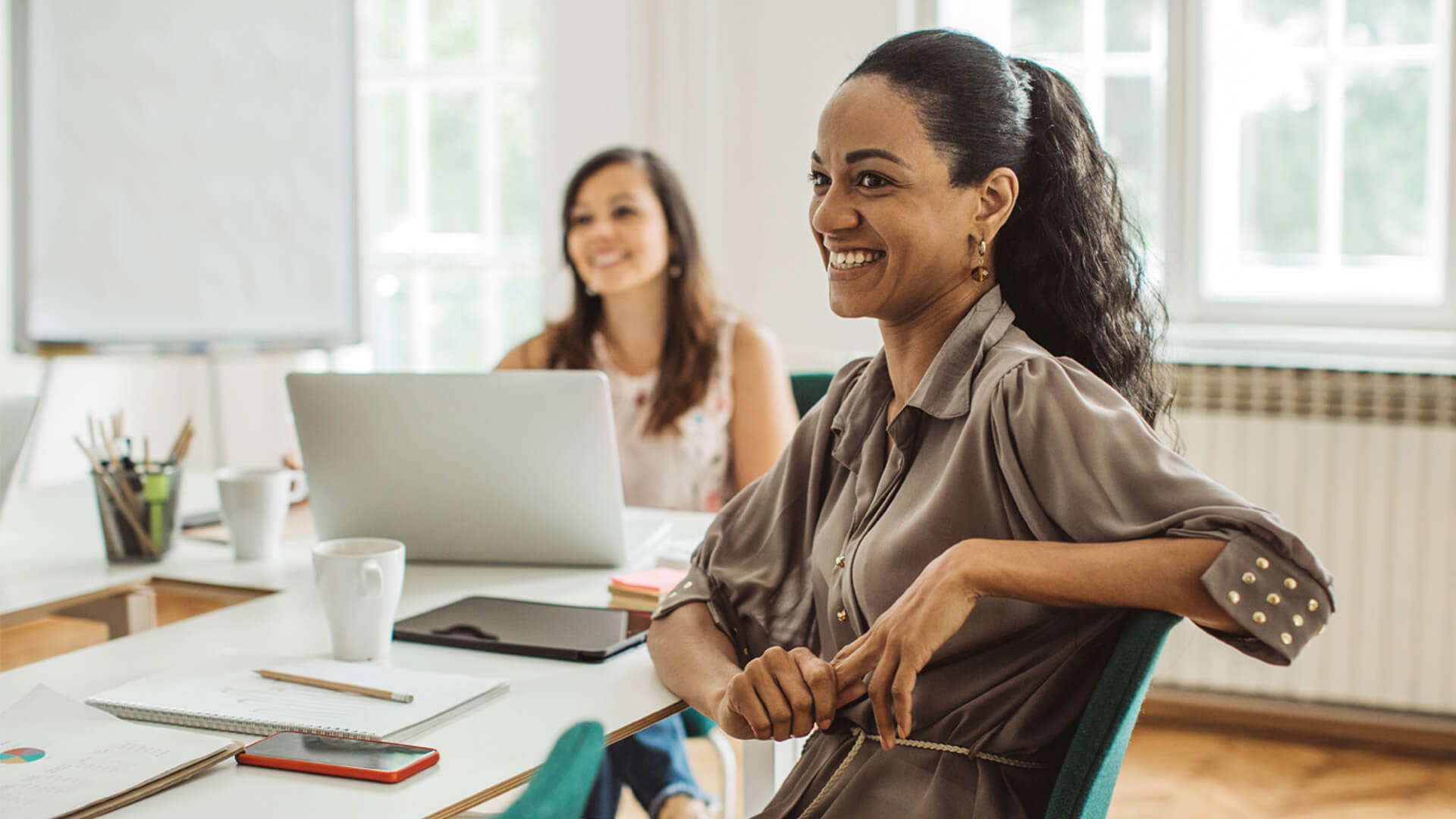 Confident woman smiling in a team setting, representing collaboration developed in the Online MBA learning experience.