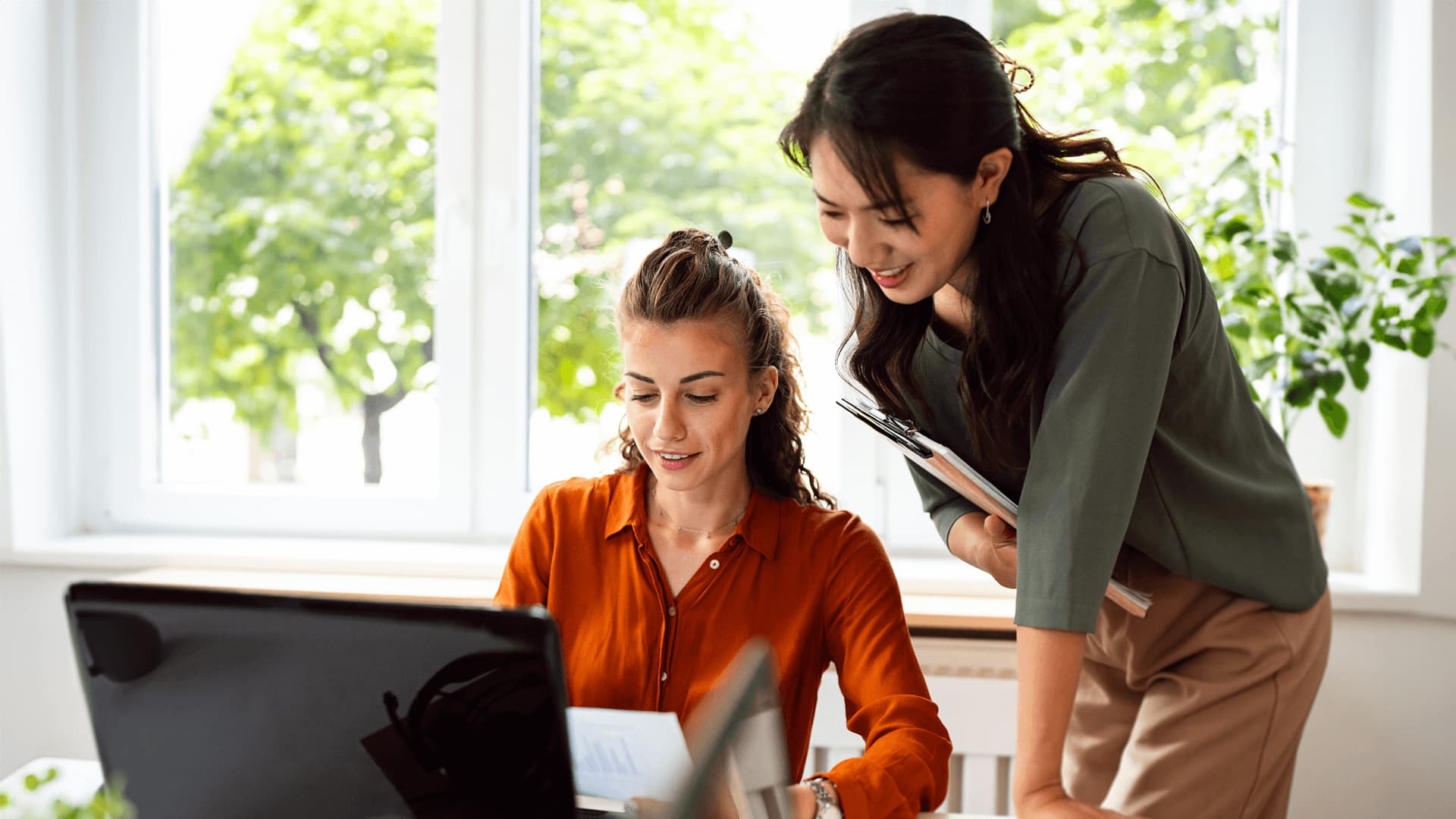 Focused MBA Project Management graduate reviews planning documents with a colleague at their desk.
