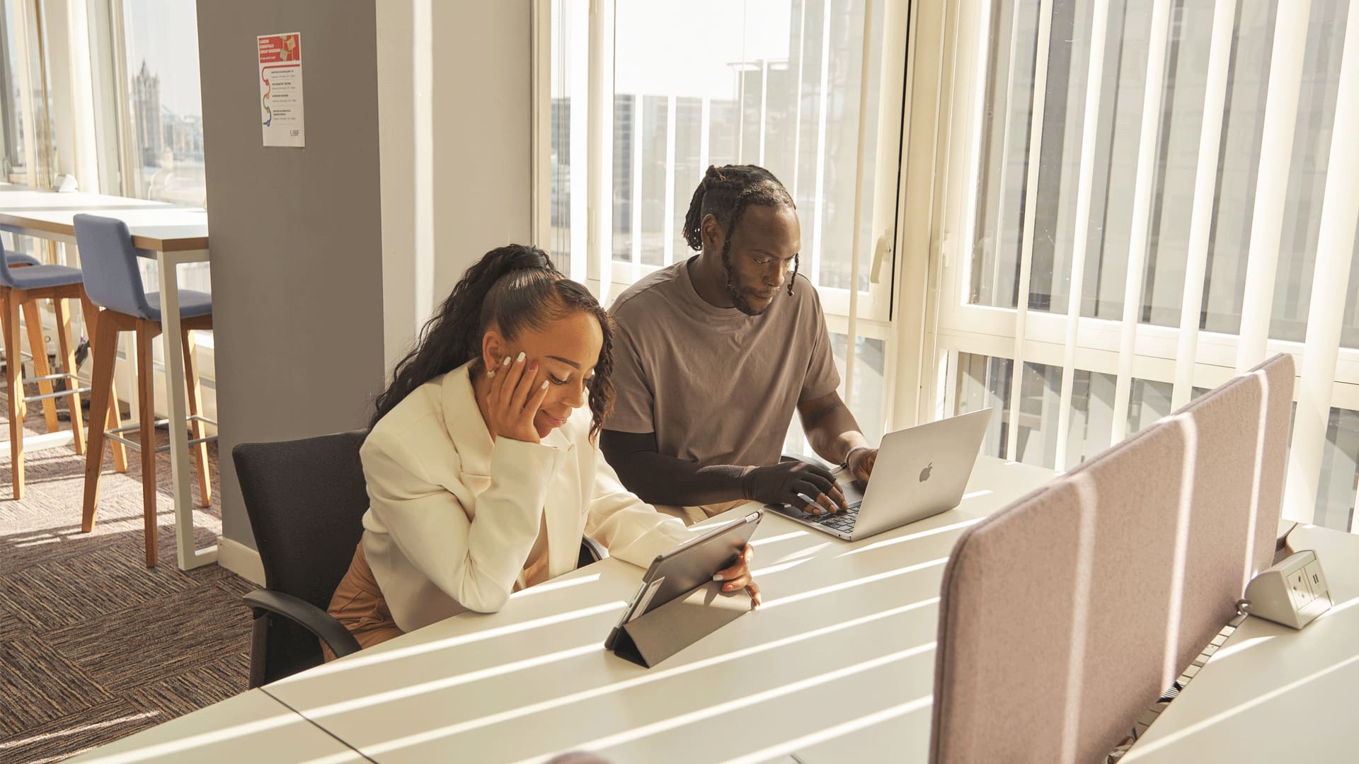 Two young adults sat at a desk looking thoughtful, applying to higher education
